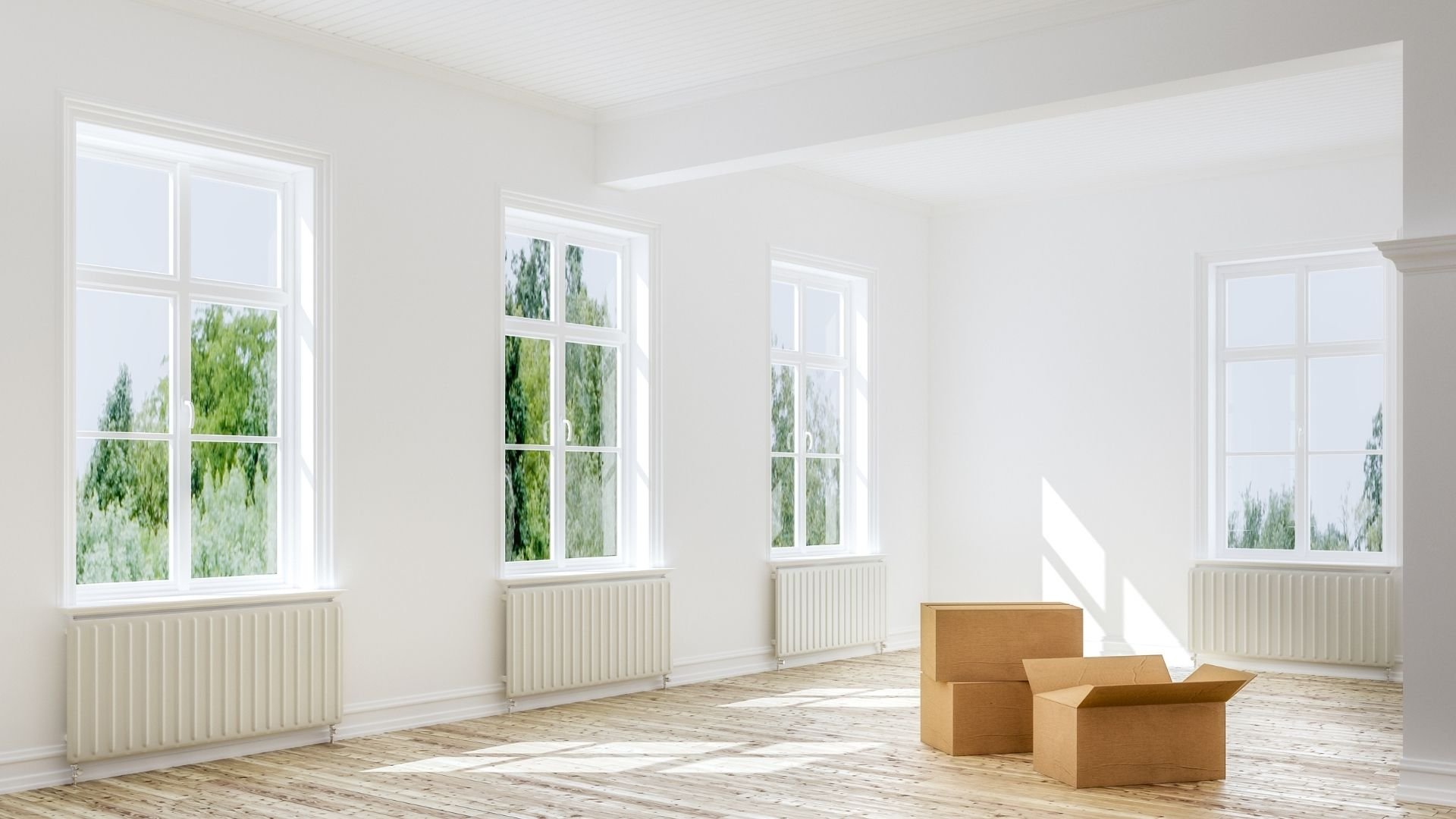 Empty room with large windows, wooden floor, and cardboard moving boxes