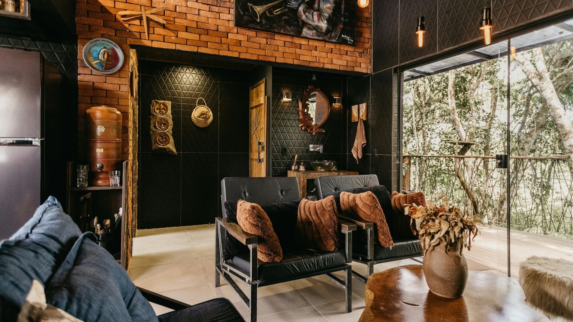 Industrial-style living room with brick walls, black leather chairs, forest view