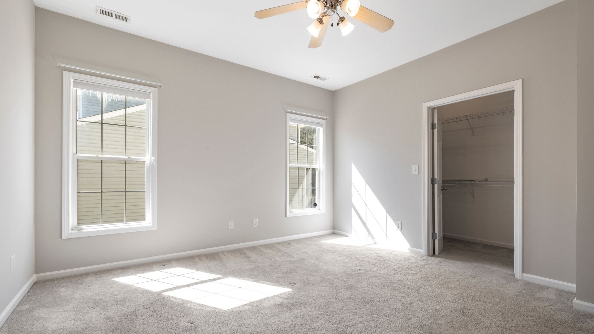 Empty bedroom with carpet, windows, and walk-in closet, ceiling fan