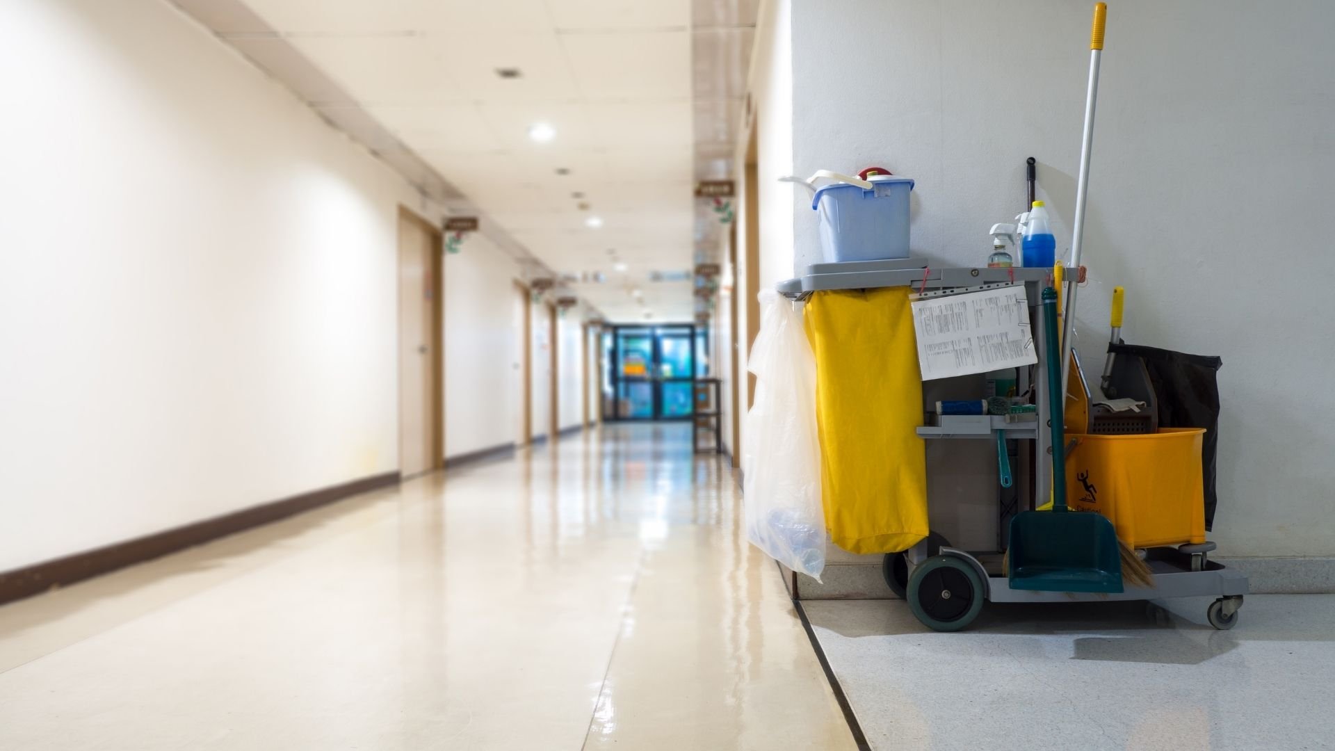 Cleaning cart with mop and supplies in empty hallway with doors