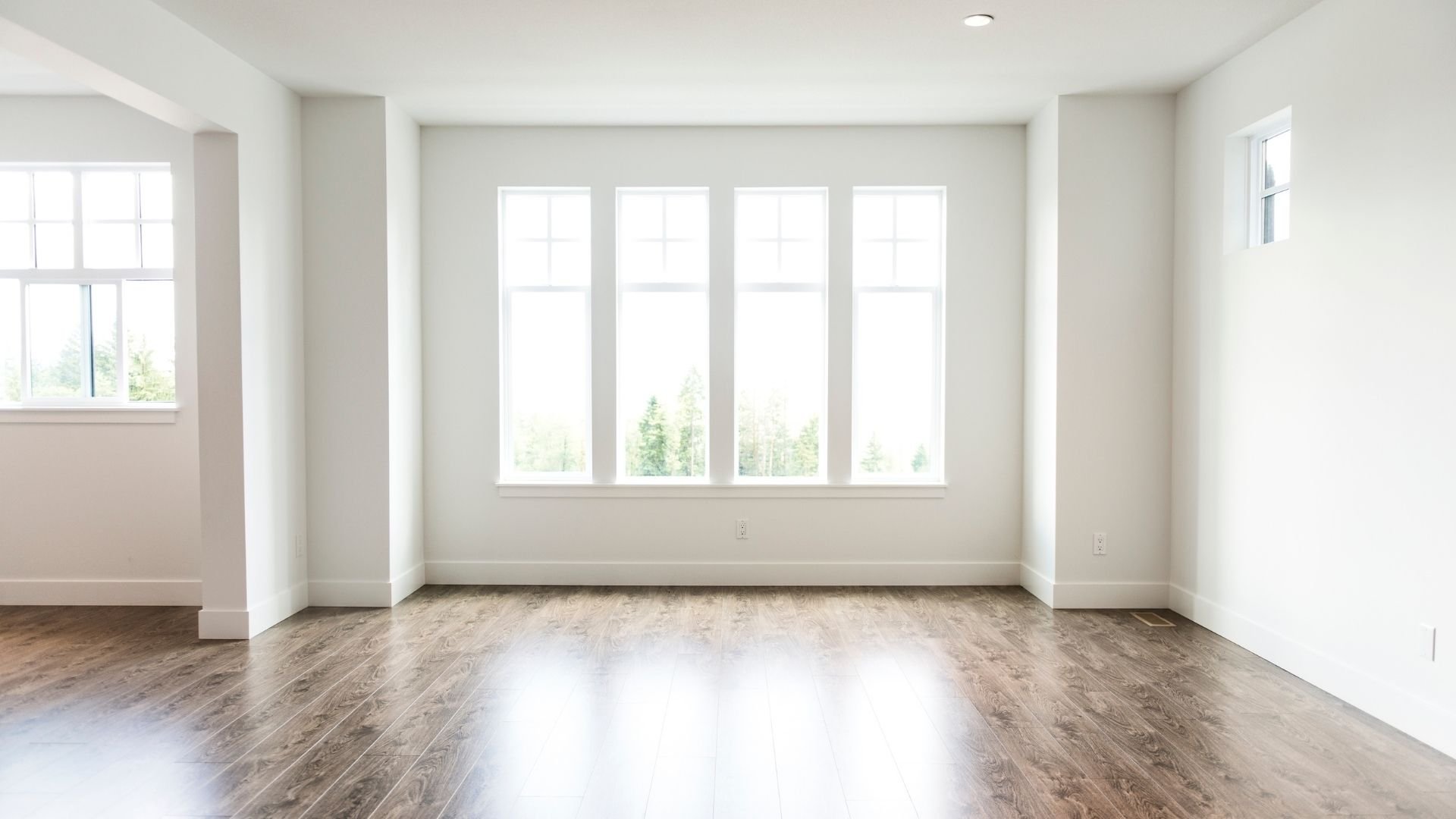 Empty white room with large windows and wooden floor, natural light