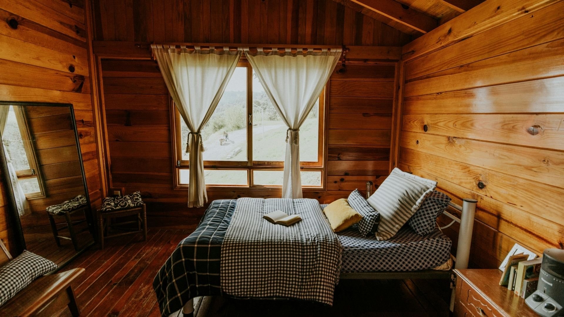 Cozy wooden cabin bedroom with checkered bedding and scenic window view