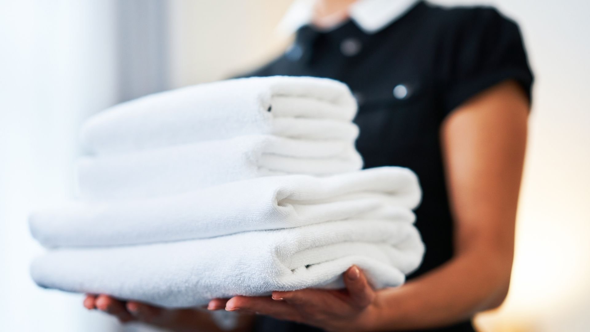Clean white towels folded neatly in hands of housekeeper